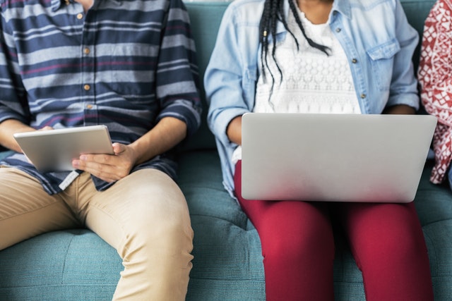 a man sitting with a tablet and a woman sitting with a laptop